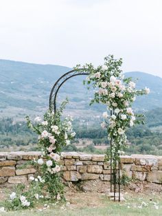 an outdoor wedding ceremony setup with white flowers and greenery on the side of a stone wall