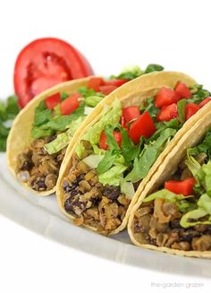 three tacos on a plate with lettuce and tomatoes