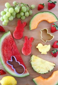 various fruits and vegetables cut into shapes on a wooden table with grapes, watermelon, kiwi, pineapple, lemons