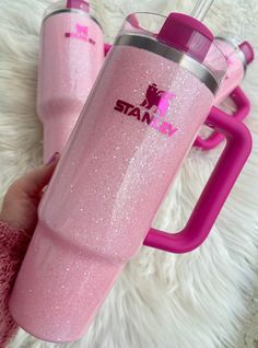 a person holding a pink tumbler next to another cup on a white carpeted floor