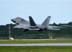 a fighter jet taking off from an airport runway with trees in the backgroud