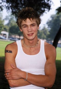 a young man with his arms crossed wearing a white tank top