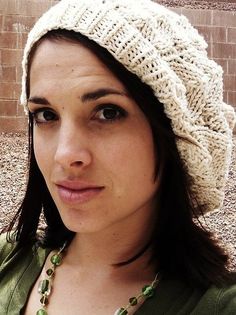 a woman wearing a white knitted hat and green shirt standing in front of a brick wall