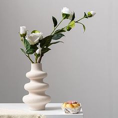 a white vase with flowers in it sitting on a table next to a cupcake