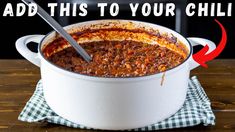 a large white pot filled with chili on top of a wooden table next to a black and white checkered napkin