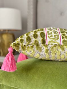 a green and white pillow with pink tassels sitting on top of a green couch