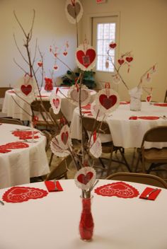 valentine's day decorations are arranged on tables in a room with white tablecloths