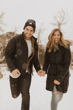 a man and woman walking in the snow holding hands