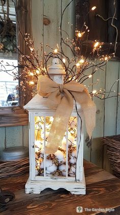 a white lantern with a bow and lights in it sitting on a table next to some branches