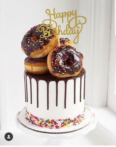 two donuts on top of a cake with chocolate and sprinkles that says happy birthday