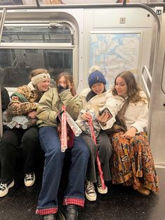 four people sitting on a subway car with their heads covered by scarves and hats