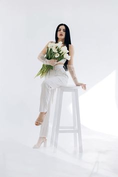 a woman sitting on top of a stool holding flowers