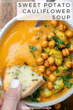 a hand holding a piece of bread over a bowl of sweet potato cauliflower soup