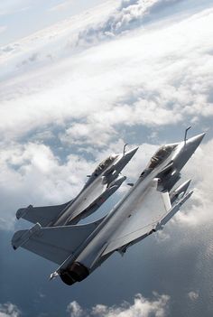 two fighter jets are flying in the sky above the clouds and water, with their landing gear down