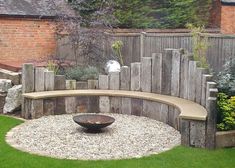 a circular bench sits in the middle of a graveled area next to a wooden fence