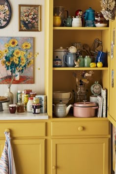 a kitchen with yellow cabinets and sunflowers on the wall above it is filled with dishes