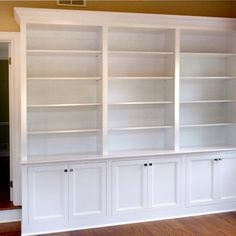 empty white bookcases in an empty room with hard wood flooring and windows