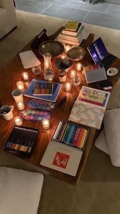 a coffee table filled with lots of books and pencils next to candles on the floor