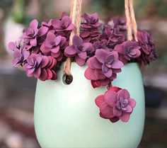 purple flowers are in a green vase hanging from twine with brown string and wooden handles