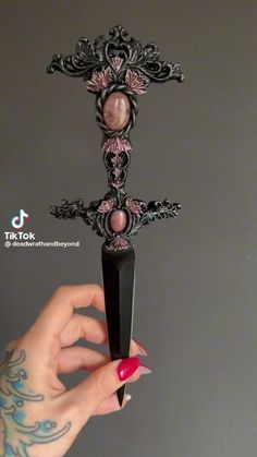 a woman's hand holding up a black cross with pink stones on the top