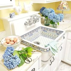 a kitchen sink with blue flowers on the counter and eggs in a bowl next to it