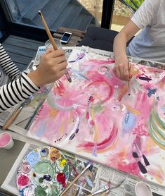 two children are painting on paper with paintbrushes and watercolors in front of them