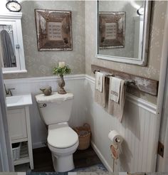 a white toilet sitting in a bathroom next to a sink under a mirror with two framed pictures above it