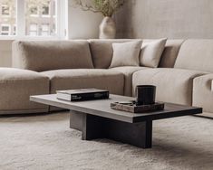 a coffee table with two books on it in front of a beige couch and window