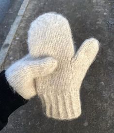 a person wearing a pair of white knitted mittens on the street with their fingers in the air