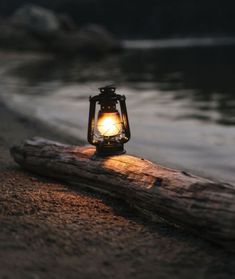 a lantern sitting on top of a wooden log next to the water with an arabic quote