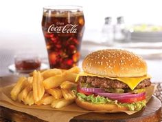 a hamburger and french fries on a wooden tray next to a glass of coke with cola in the background