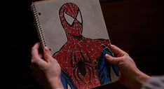 a person holding a notebook with a drawing of a spider man on it