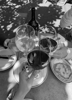 several people holding wine glasses over plates with food and drinks on them at an outdoor table