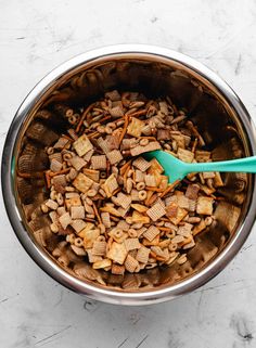 a metal bowl filled with cereal and a blue spoon in it on a marble surface