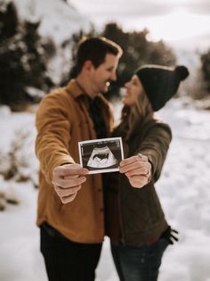 a man and woman standing in the snow holding up a polaroid frame to take a picture