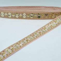 a pink ribbon with gold sequins and flowers on the edge is laying on a white surface