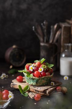 strawberries and daisies in a bowl on a cutting board next to other items