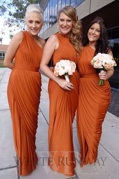 three bridesmaids in orange dresses posing for a photo with their bouquets on the street