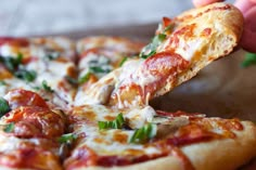 a person taking a slice of pizza from a wooden cutting board on top of a table