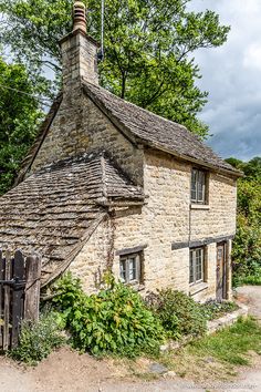 an old stone building with a wooden fence around it's perimeter and trees in the background