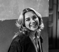 a black and white photo of a woman with blonde hair smiling at the camera while standing in front of a building