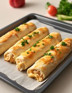 three vegetable spring rolls on a baking sheet with parsley and tomatoes in the background