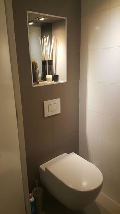 a white toilet sitting in a bathroom next to a wall mounted mirror and trash can