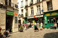 many people are walking down the street in front of stores and shops on both sides