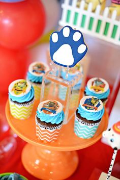 cupcakes with blue frosting and paw prints on them sitting on an orange cake stand