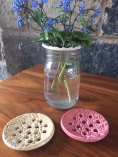 two vases with flowers in them sitting on a wooden table next to a brick wall