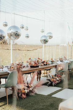 an outdoor table set up for a party with white chairs and silver balloons hanging from the ceiling