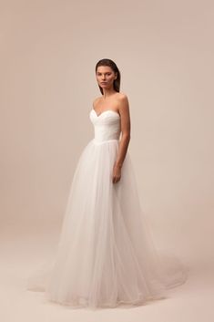 a woman in a white wedding dress standing on a beige background with her hands behind her back