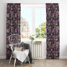 a chair and table in front of a window with purple flowers on the drapes