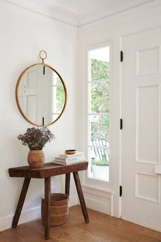 a wooden table with a mirror and vase on it in front of a white door